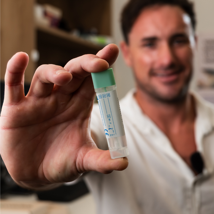 Dr. Clive Price holding a bowel cancer screening FIT Test sample bottle for stool collection with a green cap in his hand, blurred background